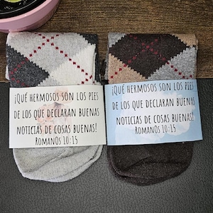May include: Two pairs of socks with a diamond pattern in gray, brown, and beige. Each sock has a card attached with a Spanish quote that reads: "¡QUÉ HERMOSOS SON LOS PIES DE LOS QUE DECLARAN BUENAS NOTICIAS DE COSAS BUENAS! ROMANOS 10:15"