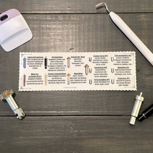 Può includere: Un primo piano di una carta bianca con illustrazioni di diversi tipi di lame da taglio per una macchina per l'artigianato. La carta è etichettata con i nomi di ogni tipo di lama in tedesco, tra cui "Follientransferwerkzeug", "Tiefschnittklinge", "Schneideroller-Klinge", "Einzelnes Falzrad #01", "Doppelfalzrad #02", "Perforationsklinge #11", "Wellenklinge #31" e "Gravurspitze #41".