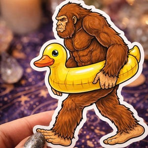 May include: A sticker featuring a brown Bigfoot carrying a yellow inflatable duck ring. The Bigfoot has a serious expression and is walking forward. The duck ring has a smiling face. The sticker is held by a hand.
