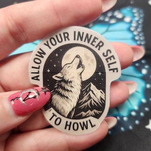 May include: A clear sticker with a black and white illustration of a howling wolf under a full moon and mountains. The sticker has the text "ALLOW YOUR INNER SELF TO HOWL" in a circular design.