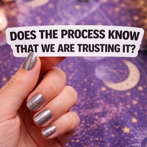 May include: A white sticker with the text "DOES THE PROCESS KNOW THAT WE ARE TRUSTING IT?" is held by a hand with silver glitter nail polish. The background is a purple celestial pattern with moons and stars.