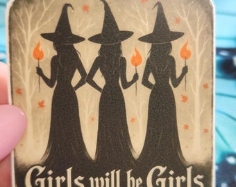 May include: A square sticker featuring three witch silhouettes holding torches against a backdrop of bare trees and orange leaves. The text "Girls will be Girls" is at the bottom in a serif font. The sticker has a vintage, slightly distressed look.