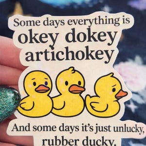 May include: A sticker featuring three yellow cartoon ducklings with orange beaks. The sticker has text that reads "Some days everything is okey dokey artichokey" and "And some days it's just unlucky, rubber ducky."