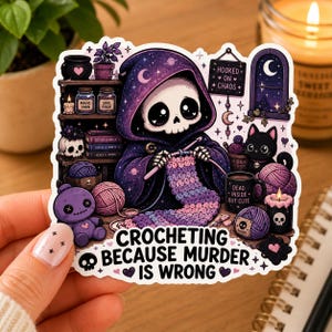 May include: A die-cut sticker featuring a skeleton in a purple hooded cloak crocheting a purple and pink project. The scene includes a black cat, yarn balls, a skull, and a sign that reads Hooked on Chaos. The text at the bottom reads Crocheting Because Murder Is Wrong.