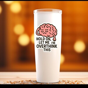 May include: A white tumbler with a humorous sticker featuring a pink brain with a hand on its head. The text on the sticker reads "Hold on, let me I'm overthink this."