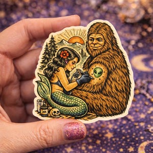 May include: A sticker featuring a mermaid tattooing a Bigfoot with an alien symbol on its chest. The mermaid has a green tail and is holding a tattoo gun. The Bigfoot is brown and furry. The sticker has a vintage, illustrative style.