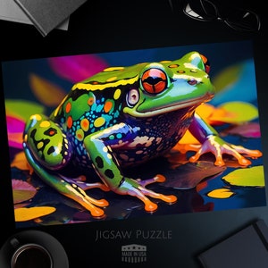 May include: A colorful jigsaw puzzle featuring a vibrant frog with green, yellow, and blue hues. The frog has orange eyes and is surrounded by colorful lily pads. The puzzle is labeled "JIGSAW PUZZLE" and "MADE IN USA".