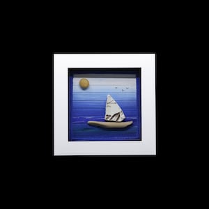May include: A framed artwork depicting a sailboat made of stones on a blue and white painted background with a yellow sun and birds.