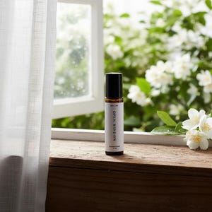 May include: A small amber glass roll-on bottle with a black cap and a white label. The label features the text "ROLL ON", "OPEN WINDOW", and "ForeverFinds 10 ml". The bottle stands upright on a wooden surface, displaying its clear, cylindrical form.