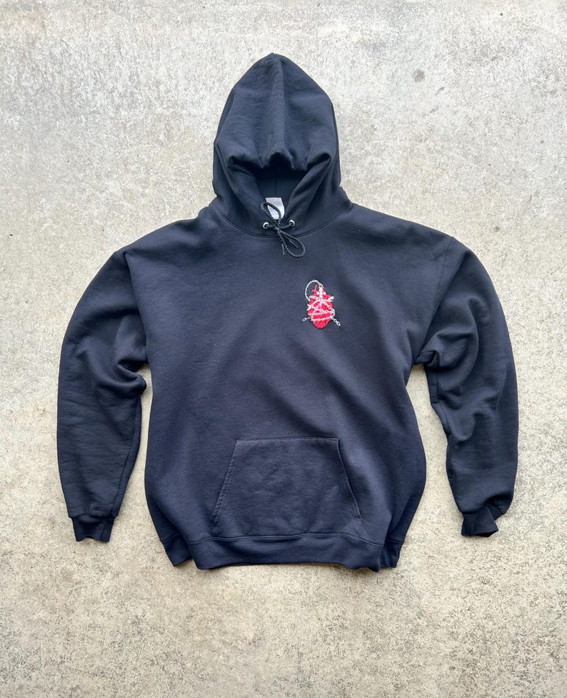 Puede incluir: Una sudadera con capucha negra con un bolsillo delantero y una capucha con cord&oacute;n. La sudadera presenta un dise&ntilde;o bordado en rojo y blanco en la parte superior izquierda del pecho. La prenda est&aacute; hecha de un material suave.