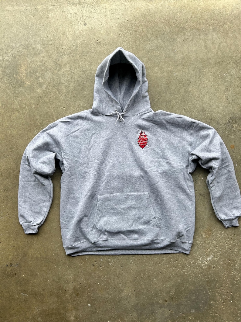 Puede incluir: Una sudadera con capucha gris con un bolsillo delantero y una capucha con cord&oacute;n. Un gr&aacute;fico rojo y blanco est&aacute; en el pecho izquierdo. La sudadera est&aacute; hecha de un material suave y c&oacute;modo.