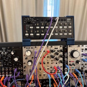 Peut inclure: Configuration de synthétiseur modulaire avec un séquenceur Korg SQ-1 noir sur un rack de modules. Des câbles de raccordement colorés relient les modules. L'ensemble comprend un Rack Brute 60 et d'autres modules.