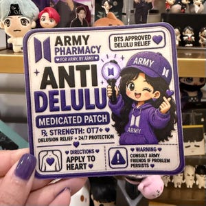 May include: A square embroidered patch with a white background and purple border. It features the text ARMY PHARMACY, ANTI DELULU, and MEDICATED PATCH. An illustration of a character in a purple hoodie and cap holds a light stick. Includes text: BTS APPROVED DELULU RELIEF, RX STRENGTH: OT7+, 24/7 PROTECTION, APPLY TO HEART, and CONSULT ARMY FRIENDS IF PROBLEM PERSISTS.