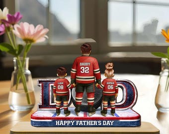 Könnte beinhalten: Eine Hockey-Figur zum Vatertag. Sie zeigt einen Vater und zwei Kinder in Hockey-Trikots, die auf einer Hockey-Rink-Basis stehen. Das Wort "DAD" wird zusammen mit dem Text "HAPPY FATHER'S DAY" angezeigt. Die Figur steht auf einem Holzsockel.