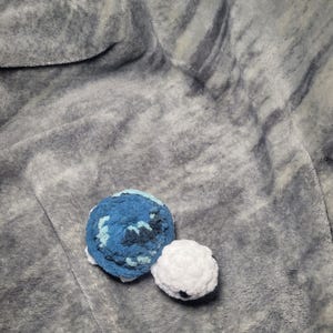 May include: A crocheted blue and white turtle toy on a grey fluffy blanket.