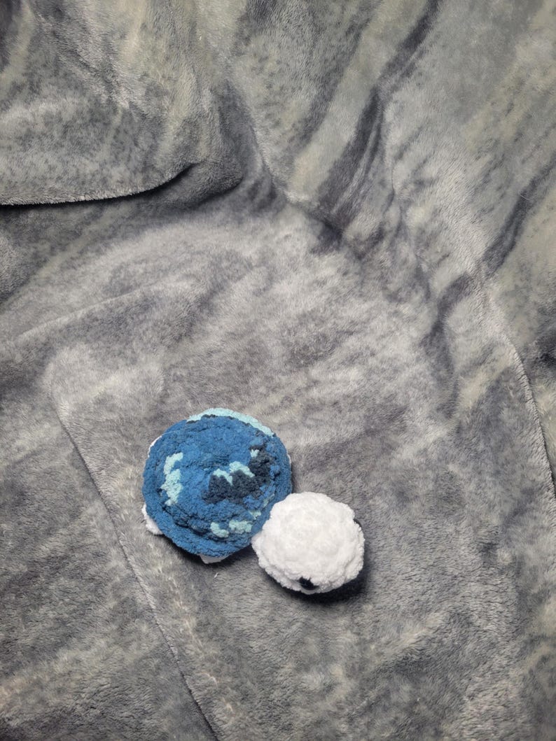 May include: A crocheted blue and white turtle toy on a grey fluffy blanket.