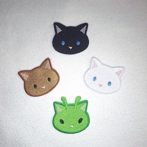 May include: Four embroidered cat face patches in black, brown, white, and green. Each patch features a cat face with embroidered details, including eyes and a nose. The patches are arranged in a circular pattern against a white background.