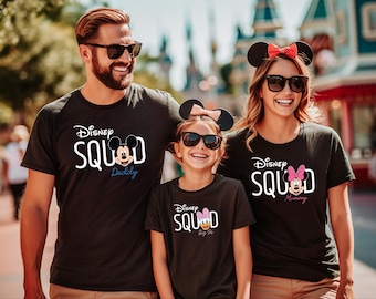 Puede incluir: Tres personas vestidas con camisetas negras con la frase "Disney Squad". Las camisetas presentan gráficos de Mickey Mouse, Minnie Mouse y Daisy Duck, con las palabras "Daddy", "Mummy" y "Big Sis". Todos llevan gafas de sol.