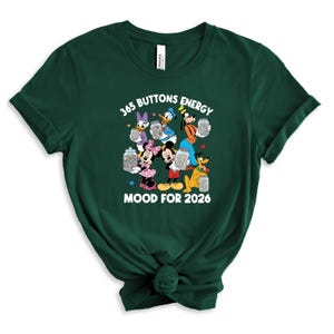 May include: Dark green t-shirt with a graphic of Disney characters, including Mickey and Minnie Mouse, Donald Duck, and Goofy. The text reads "365 Buttons Energy Mood for 2026". The design includes colourful buttons in jars.