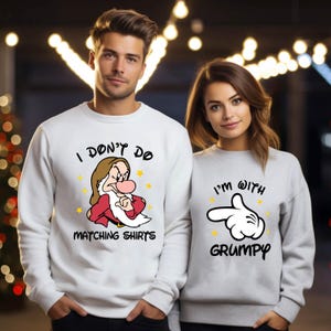 May include: Matching white and grey sweatshirts with cartoon graphics. One sweatshirt says "I don't do matching shirts" with a Grumpy cartoon character. The other says "I'm with Grumpy" with a pointing hand graphic. Yellow stars are also featured.