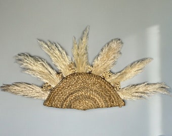 May include: A wall decor piece made of dried pampas grass arranged in a half-circle shape with a woven straw base.