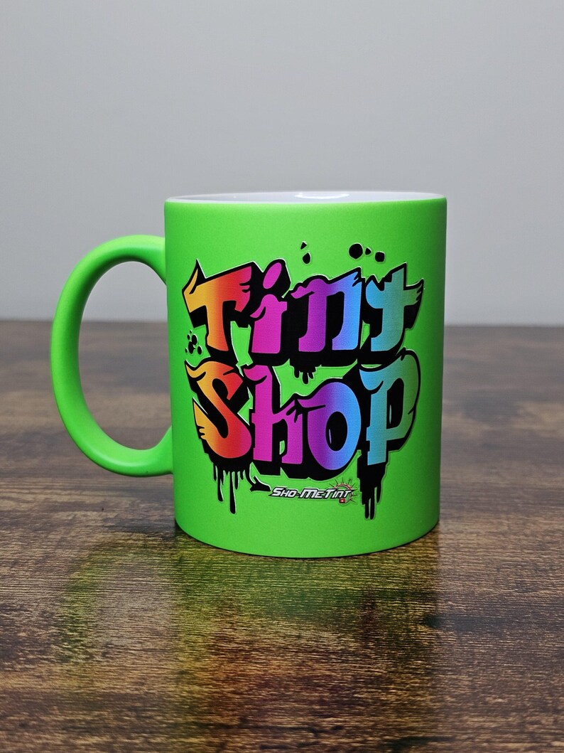 May include: A green ceramic mug with a colorful graffiti-style design that says "Tiny Shop" with the words "Sho-Me-Tiny" underneath.