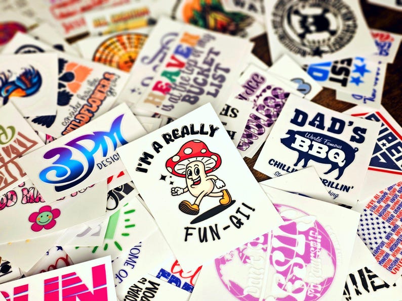 May include: Assortment of colorful temporary tattoos with various designs, including a mushroom character with the text "I'm a really fun-gi!" and a BBQ design with the text "Dad's World Famous BBQ Chillin' & Grillin' King".