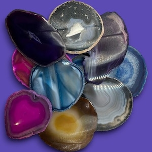 May include: A collection of agate slices in various colors and patterns, including purple, pink, blue, and brown. The slices are arranged in a pile, with the largest slice at the top.