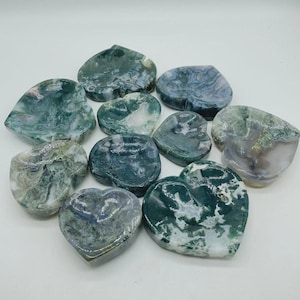 May include: A collection of heart-shaped stones in shades of green, white, and gray. The stones have a marbled appearance, with varying patterns and textures. The arrangement is scattered, showcasing the natural beauty of the polished gemstones.