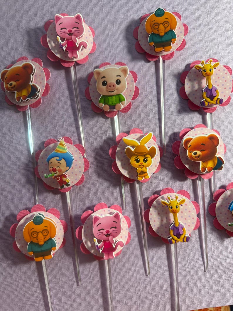 Pu&ograve; includere: Topper per cupcake con vari personaggi dei cartoni animati. Ogni topper ha una base a forma di fiore rosa con un centro a pois e uno stelo trasparente. I personaggi includono un orso, un maiale, una giraffa e altri.