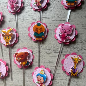 Pu&ograve; includere: Decorazioni per cupcake con disegni di personaggi dei cartoni animati. Ogni decorazione ha un'immagine del personaggio su un cerchio rosa a pois, circondato da un bordo smerlato rosa, attaccato a un bastoncino di plastica trasparente.