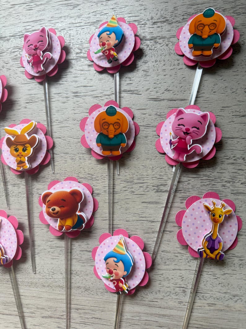 Pu&ograve; includere: Decorazioni per cupcake con disegni di personaggi dei cartoni animati. Ogni decorazione ha un'immagine del personaggio su un cerchio rosa a pois, circondato da un bordo smerlato rosa, attaccato a un bastoncino di plastica trasparente.