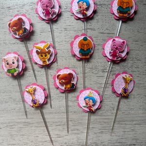 Pu&ograve; includere: Una collezione di decorazioni per cupcake con vari personaggi di animali dei cartoni animati. Ogni decorazione ha un bordo smerlato rosa con un motivo a pois e un bastoncino di plastica trasparente. I personaggi includono un orso, un gatto, un maiale, una giraffa e un clown.