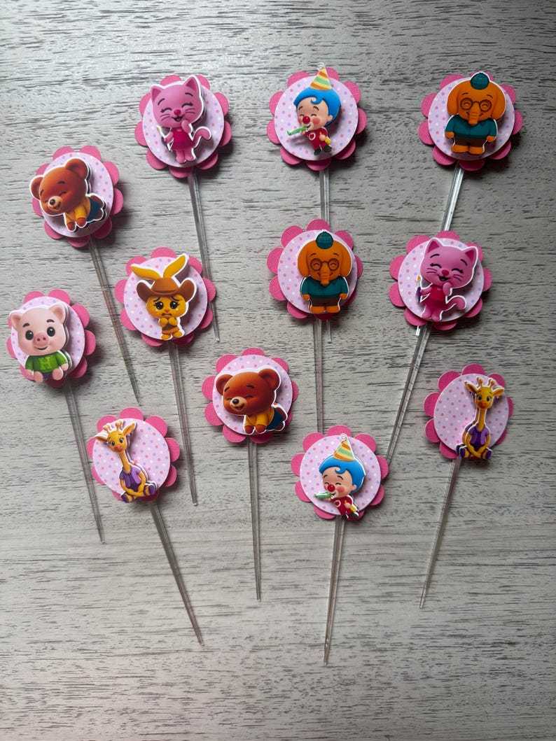 Pu&ograve; includere: Una collezione di decorazioni per cupcake con vari personaggi di animali dei cartoni animati. Ogni decorazione ha un bordo smerlato rosa con un motivo a pois e un bastoncino di plastica trasparente. I personaggi includono un orso, un gatto, un maiale, una giraffa e un clown.