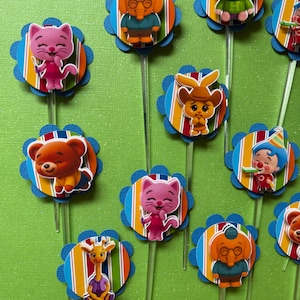 May include: A collection of colorful cupcake toppers featuring various cartoon animal characters. Each topper has a blue scalloped edge, a striped center, and a clear plastic stick. The characters include a pig, cat, bear, elephant, and giraffe.