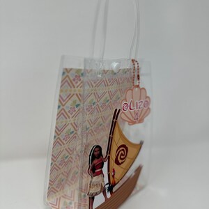 Może przedstawiać: Przezroczysta plastikowa torba z nadrukiem przedstawiającym polinezyjską kobietę z kogutkiem na łodzi. Torba ma biały uchwyt i r&oacute;żową metkę z tekstem "@Lizo 4".