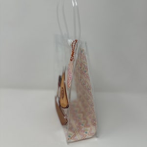 Może przedstawiać: Przezroczysta plastikowa torba z nadrukiem brązowego i białego żaglowca. Torba ma uchwyt i zamek błyskawiczny.