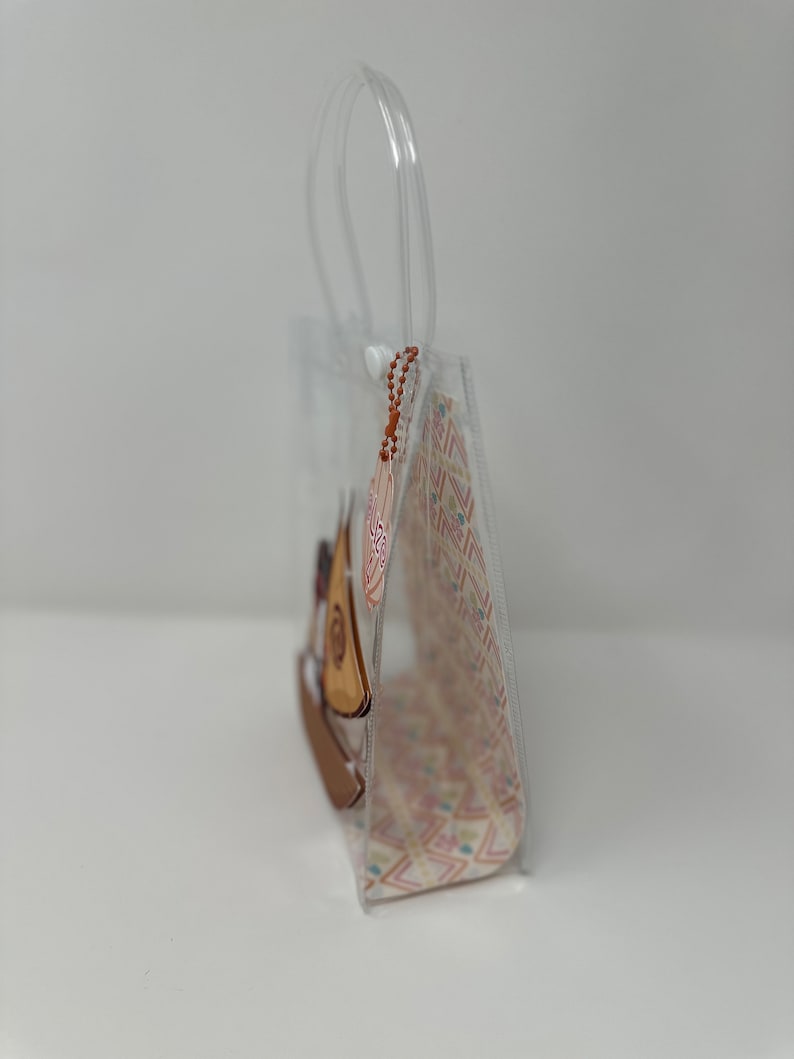 Może przedstawiać: Przezroczysta plastikowa torba z nadrukiem brązowego i białego żaglowca. Torba ma uchwyt i zamek błyskawiczny.