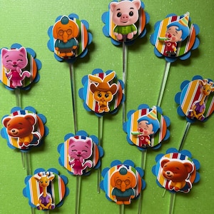 May include: A collection of colorful cupcake toppers featuring various cartoon animal characters. Each topper has a blue scalloped edge, a striped background, and a clear plastic stick.