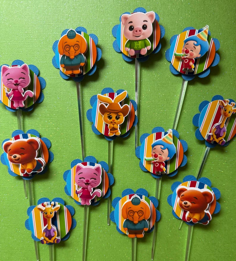 May include: A collection of colorful cupcake toppers featuring various cartoon animal characters. Each topper has a blue scalloped edge, a striped background, and a clear plastic stick.