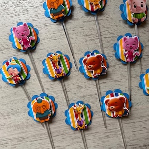 May include: A collection of colorful cupcake toppers featuring various cartoon animal characters. Each topper has a blue scalloped edge, a striped background, and a clear plastic stick.