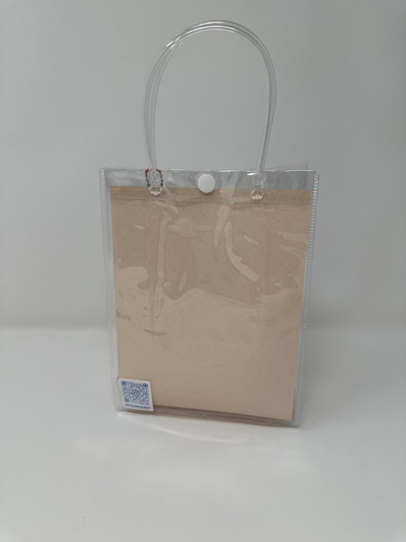 Może przedstawiać: Przezroczysta plastikowa torba z białym zapięciem na guzik i brązową wkładką papierową. Torba ma przezroczysty plastikowy uchwyt.