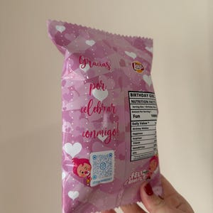 May include: A pink Lay's potato chip bag with white hearts and text in Spanish. The text reads "Gracias por celebrar conmigo!" and "Felicidades". The bag also has a QR code and a cartoon character.