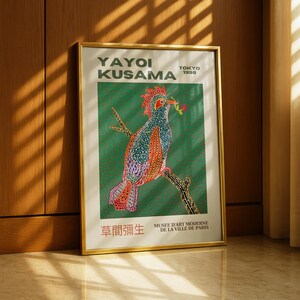 Könnte beinhalten: Ein gerahmter Kunstdruck mit einer farbenfrohen Vogelillustration von Yayoi Kusama. Der Vogel, mit rotem Kamm und gemusterten Federn, sitzt auf einem Ast vor grünem Hintergrund. Der Druck enthält Text auf Englisch, Japanisch und Französisch.