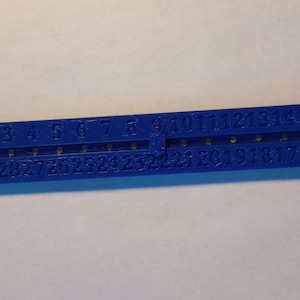 May include: Blue plastic ruler with numbers 1 through 30 printed on it. The ruler has a loop on the end.