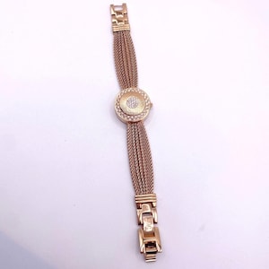 Peut inclure: Une montre-bracelet dorée avec un cadran rond et un bracelet en forme de chaîne. Le cadran de la montre est orné de petits cristaux scintillants sur le pourtour et d'un groupe de cristaux au centre. Le bracelet est composé de plusieurs chaînes fines.