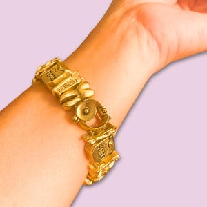 May include: A gold charm bracelet with various charms, including a heart, a bell, and a building with the text "LOVE YOU" on it.