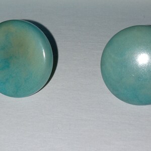 May include: A pair of round, turquoise-colored earrings with a subtle marbled pattern.