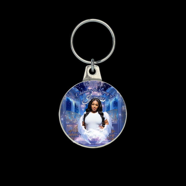 Puede incluir: Un llavero redondo plateado con un colgante circular. El colgante muestra a una mujer con alas de &aacute;ngel sobre un fondo azul. El texto dice "Celebrating the Legacy of Jasmine". La mujer lleva una camiseta blanca.