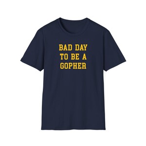May include: Navy blue t-shirt with the text "BAD DAY TO BE A GOPHER" in yellow block letters. The shirt is a short-sleeved crew neck style, suitable for casual wear. The text is centered on the chest.